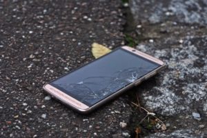 Smartphone mit zerbrochenem Display auf gebrochenem Asphalt